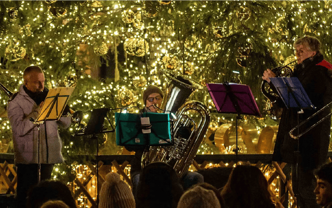 Bläserensemble spielt Weihnachtsmusik vor dem beleuchteten Christbaum am Weihnachtsmarkt Schloss Schönbrunn
